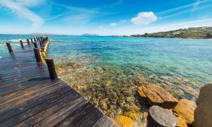 a picture of the wooden pier at romazzino beach in costa smeralda sardinia