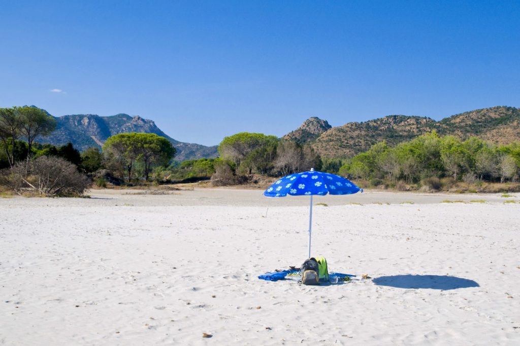 a picture of a blue umbrella on the beach named Spiaggia sa Curcurica, in Orosei, east Sardinia, Italy.