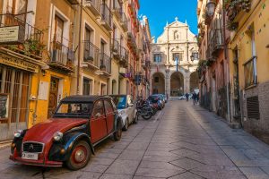 Street view with old houses, Church and Vestry of Saint Michele and vintage red car on Via Domenico Alberto Azuni