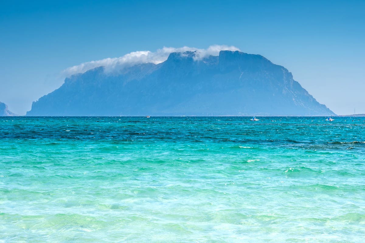 a picture of cloud-covered Isola Tavolara, seen from a beach at Murta Maria, a seaside village in north-east Sardinia, Italy.