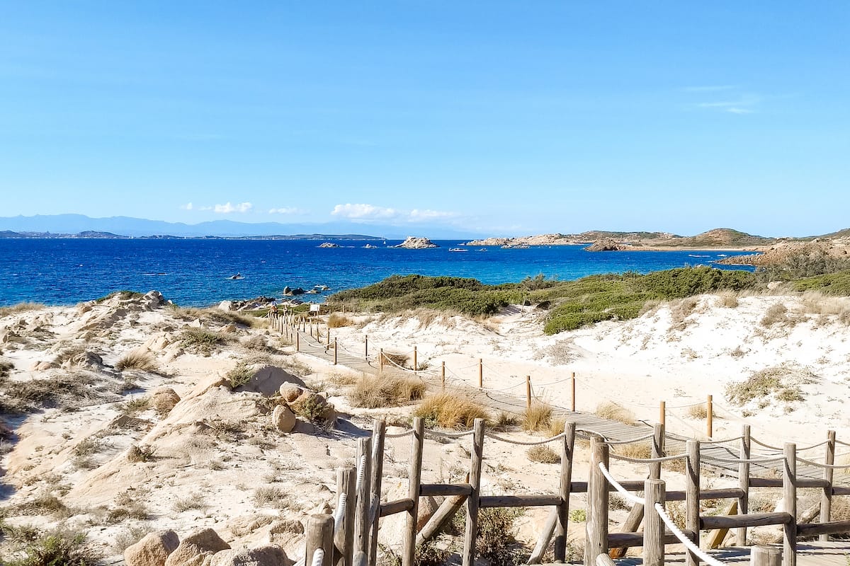 Spiaggia di Bassa Trinita, where a wooden pathway winds through a patch of dunes and Mediterranean vegetation, adding to the natural charm of the location.